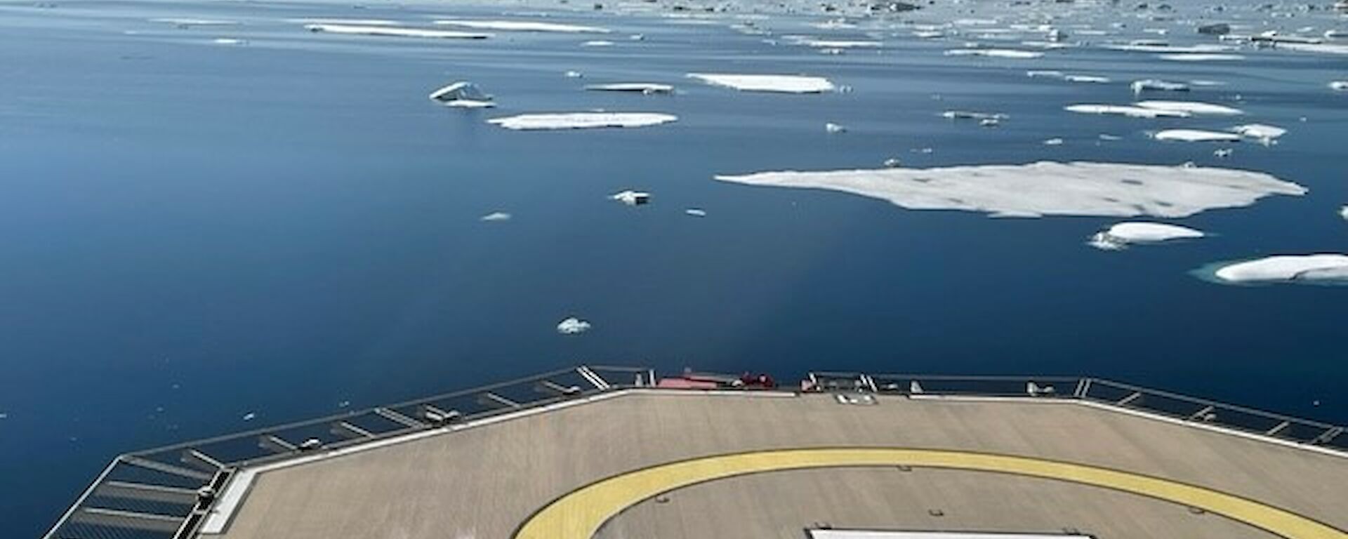 A heli-deck on the back of a ship with icebergs and water in the background