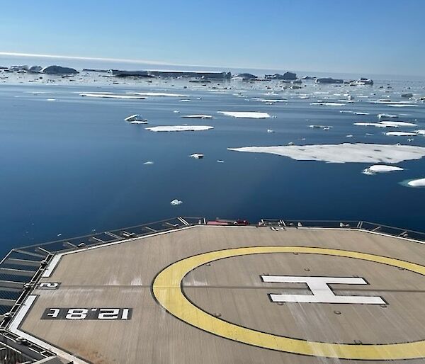 A heli-deck on the back of a ship with icebergs and water in the background