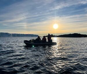 A small boat in the water with a large glacier and sun setting in the background