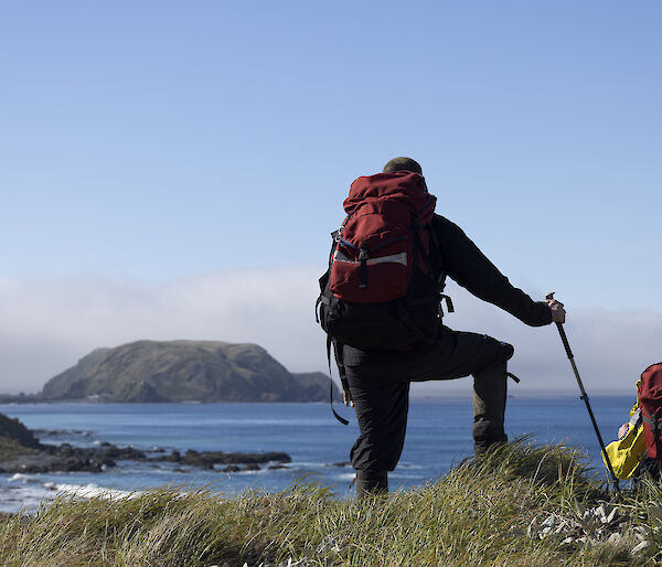 Two hikers overlook a blue bay from a grassy tussock