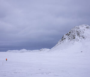 A snow covered landscape has a solitary person in red walking into the distance