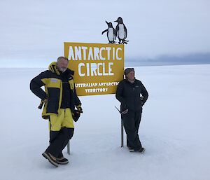Rebecca stands next to actor Sam Neill at a sign that says Antarctic Circle