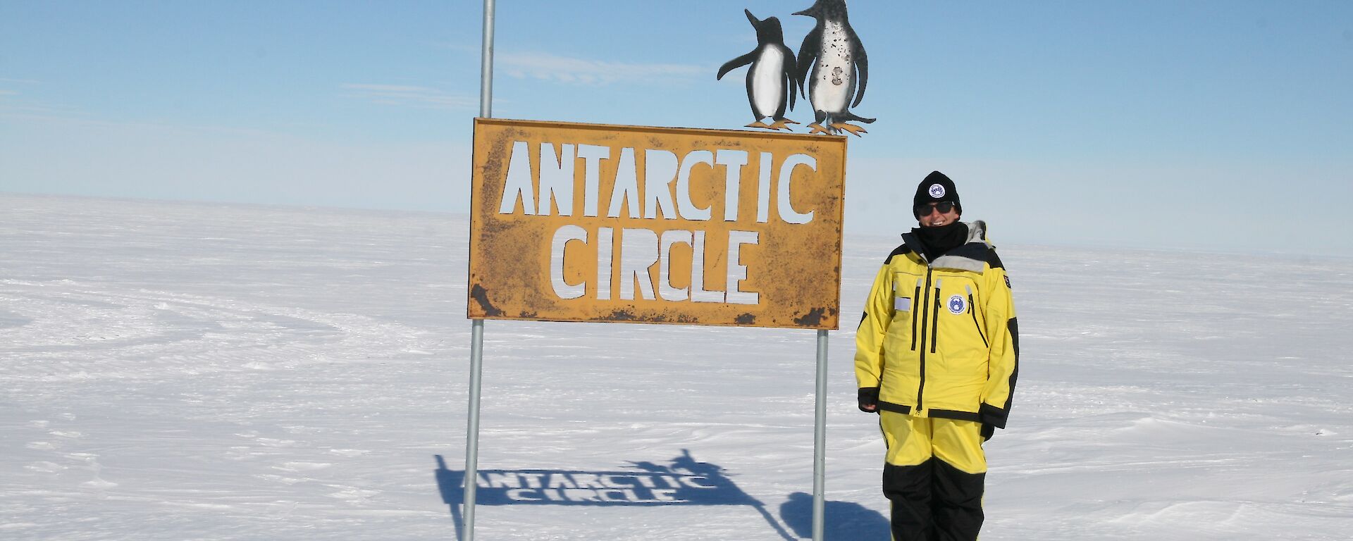 A woman stands next to a sign that reads Antarctic Circle