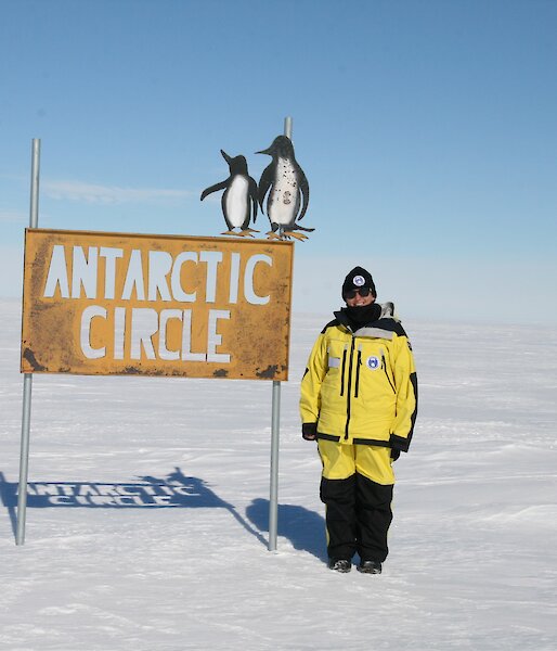 A woman stands next to a sign that reads Antarctic Circle