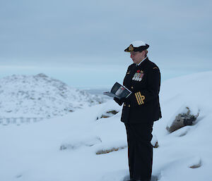 A woman in uniform reads from a piece of paper surrounded by snow