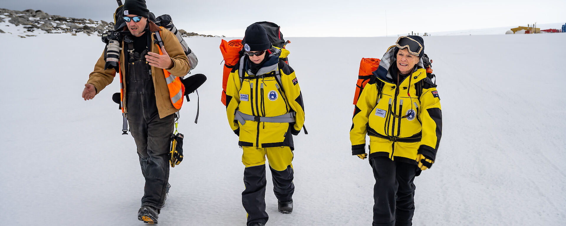 three people walk across snow