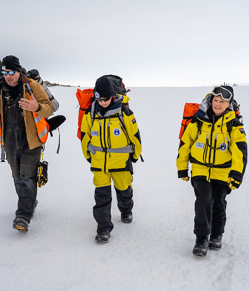 three people walk across snow