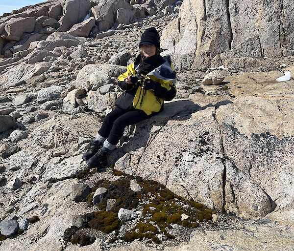 woman sits on rock taking photo of moss bed