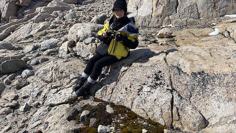 woman sits on rock taking photo of moss bed