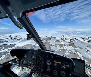 An aerial view of snow and rocks from pilots seat in a helicopter