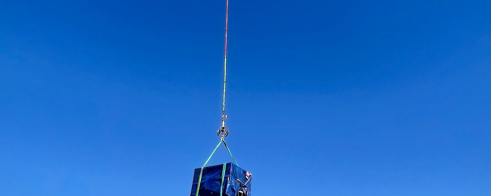 A helicopter carrying a blue cage on a long rope