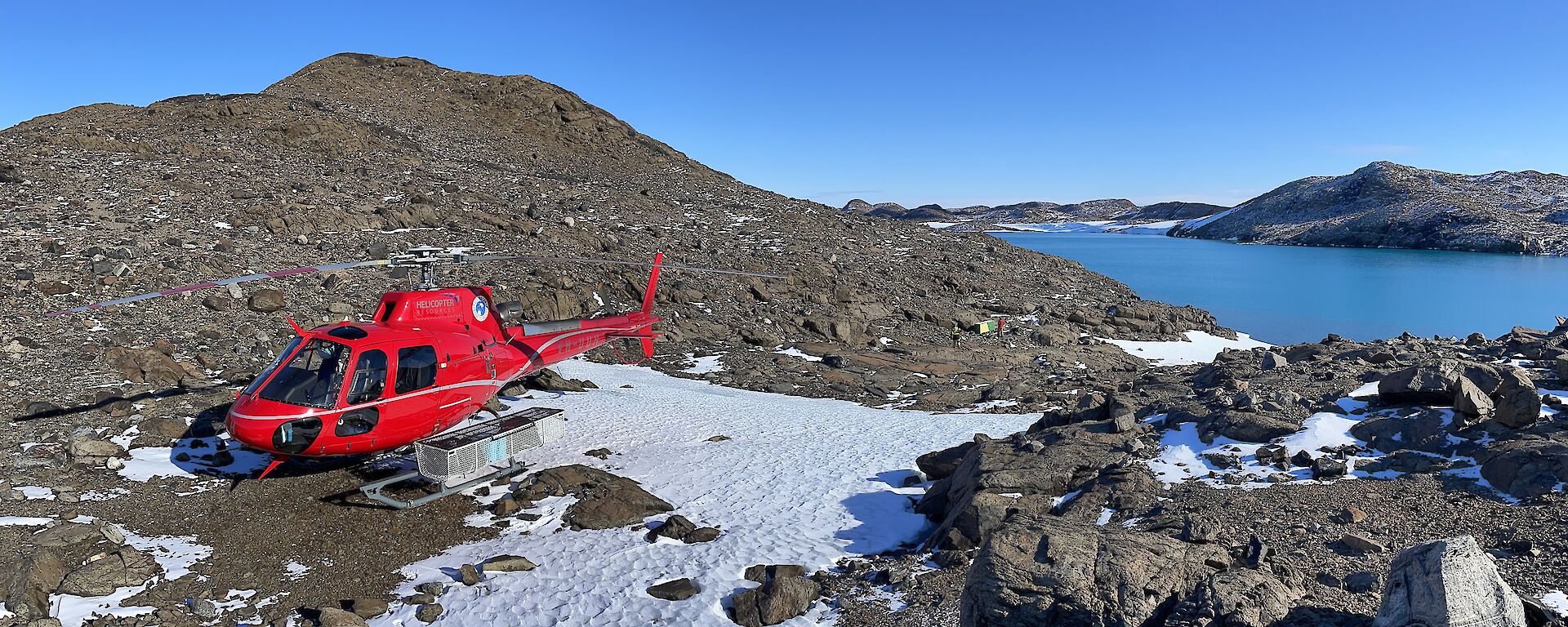 A red helicopter sits atop rocks and snow