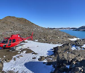 A red helicopter sits atop rocks and snow