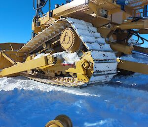 A large bulldozer, painted yellow, with a good deal of snow caught in its wheels and treads