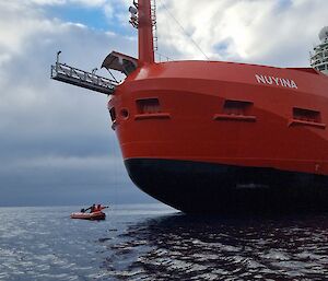A man in an inflatable boat reaches for rope dangling from a massive ship