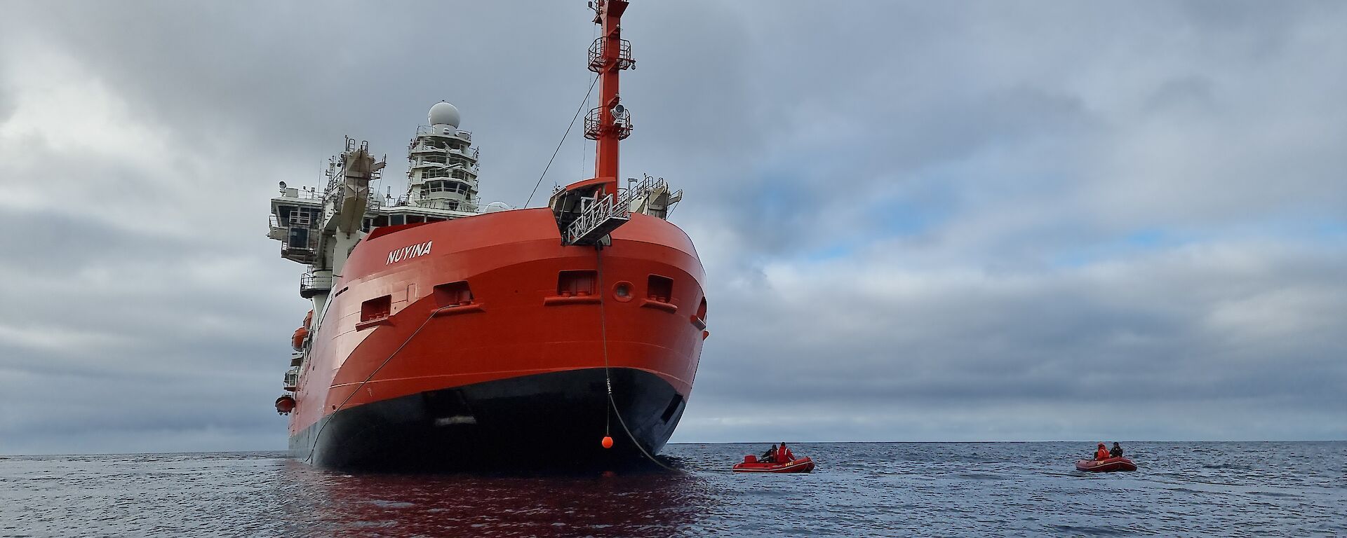 A massive red ship sits in the ocean with smaller boats next to it