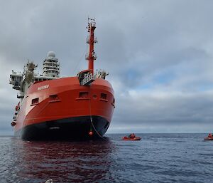 A massive red ship sits in the ocean with smaller boats next to it