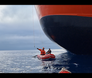 A man in an inflatable boat reaches for rope dangling from a massive ship
