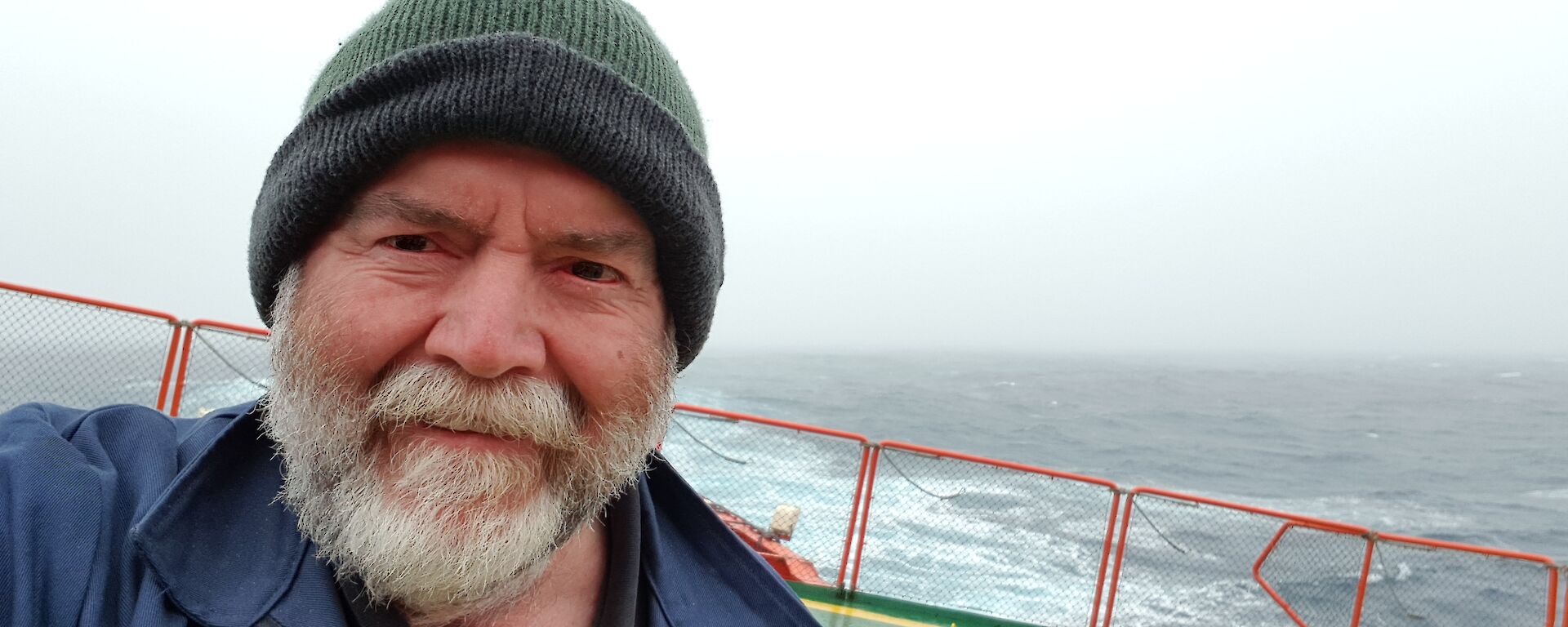 A man in a green beanie taking a selfie standing on the back of a ship