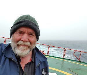 A man in a green beanie taking a selfie standing on the back of a ship