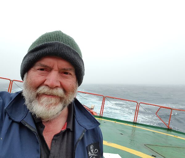 A man in a green beanie taking a selfie standing on the back of a ship