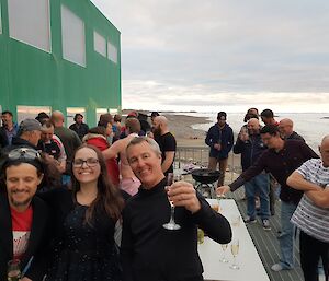 A group of people standing on a metal deck with a green building and snow in the background