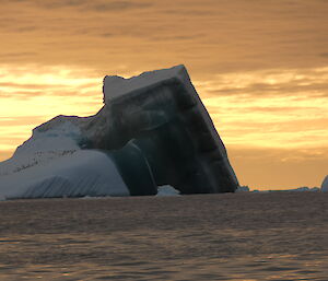 A jade iceberg with penguins sitting on it with a sunset in the background