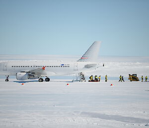 People in yellow survival outfits walk away from a plane parked on the ice runway