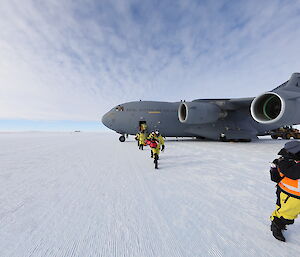 People in yellow survival gear walk away from a massive grey aircraft