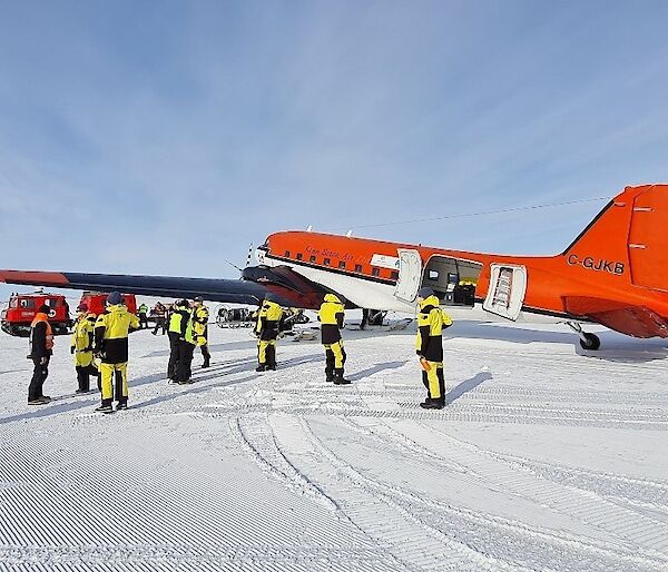 A red plane parked on the ice surrounded by people in yellow survival gear