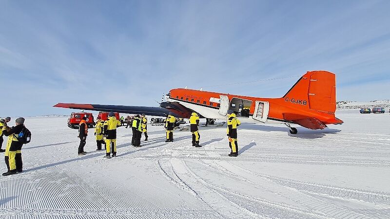 A red plane parked on the ice surrounded by people in yellow survival gear