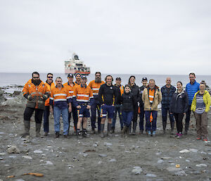 A group of expedititioners standing with the ocean and an icebreaker behind them