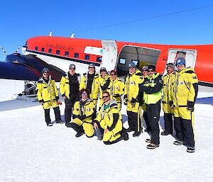A group of expeditioners in yellow survival clothing standing outside a Basler aircraft