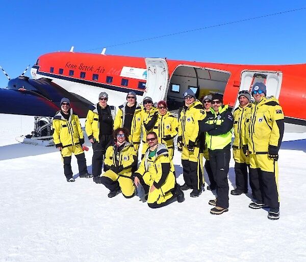 A group of expeditioners in yellow survival clothing standing outside a Basler aircraft