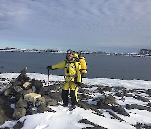 Man standing with a backpack amongst rocks and snow with water in the background