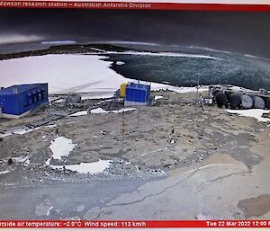 Harbour in middle of picture half covered in sea-ice, in foreground rocky land and two blue buildings and fuel farm