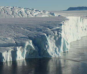 Ice cliffs formed by glacier rolling into the water of a bay. Blue sky sunny day. Water of bay at front of picture is deep blue and calm.