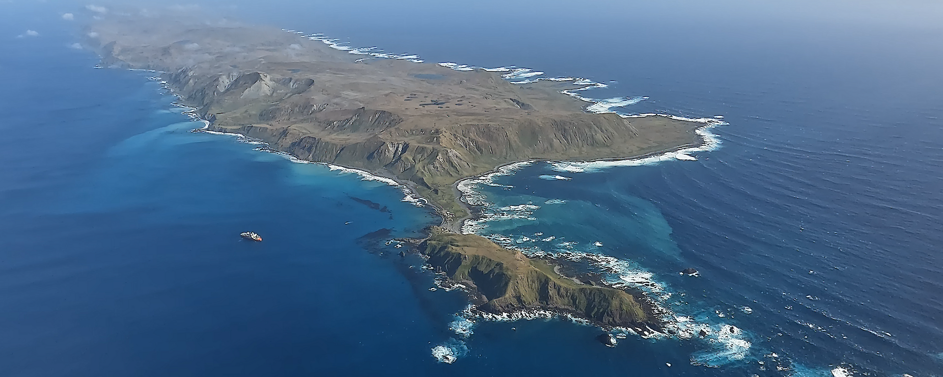 An aerial view of a red ship next to a mountainous island