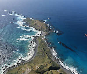 An aerial view of a red ship next to a mountainous island, with a research station in view