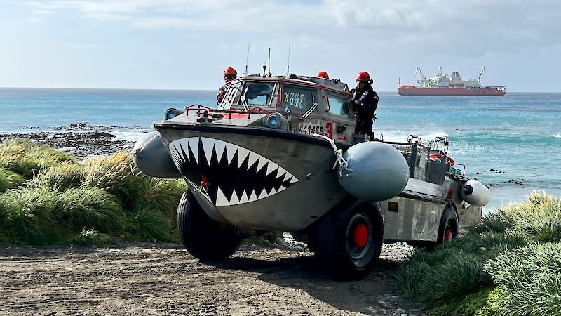 An amphibious boat on wheels with teeth painted on the front crosses the beach