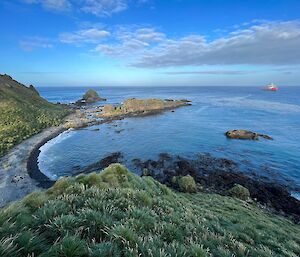 A small bay surrounded by green vegetation with a red ship out at sea