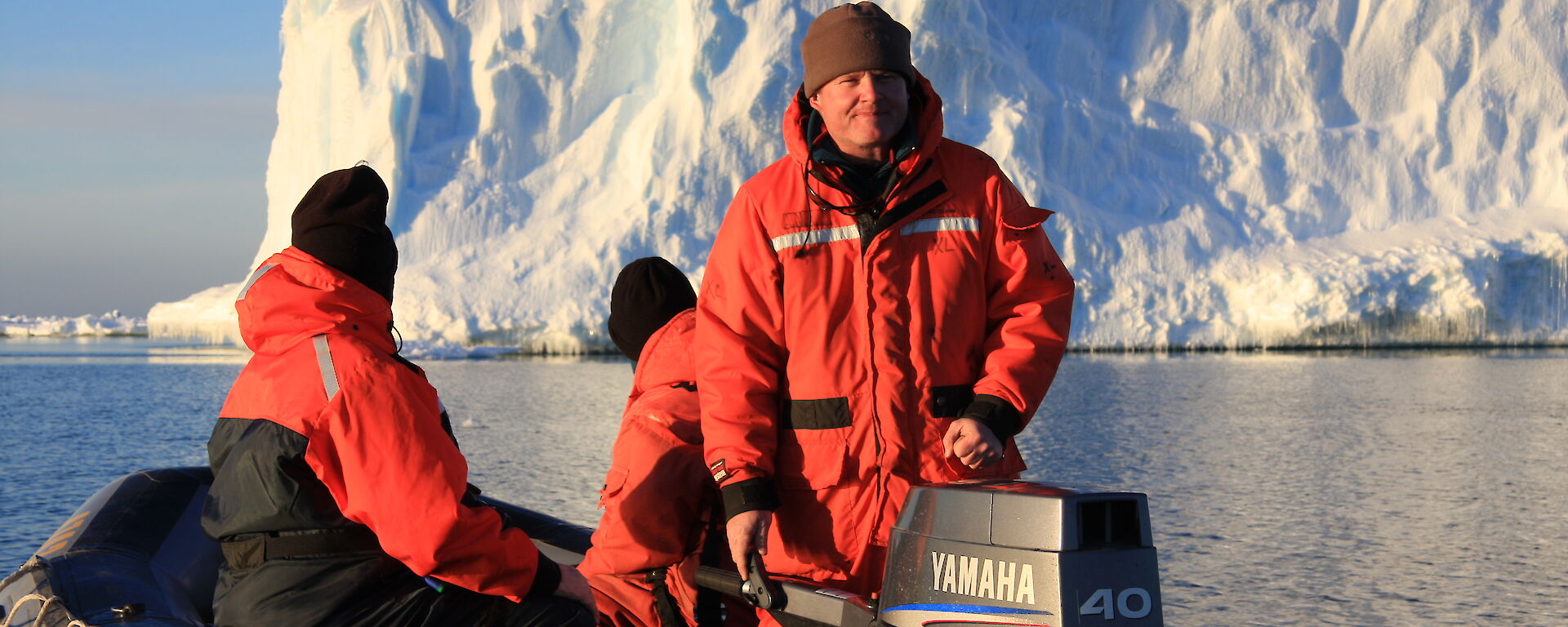 A man on a boat in Antarctica with an ice cliff behind him