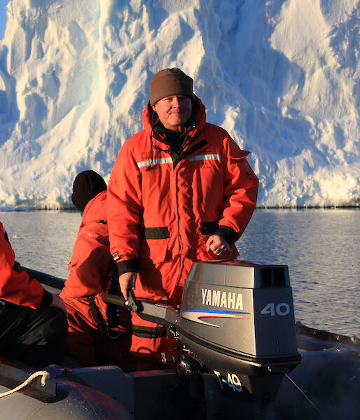 A man on a boat in Antarctica with an ice cliff behind him