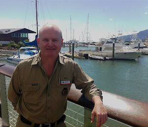 A man smiling with a marina and boats behind him