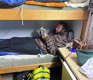 Man lies on bottom bunk reading a book