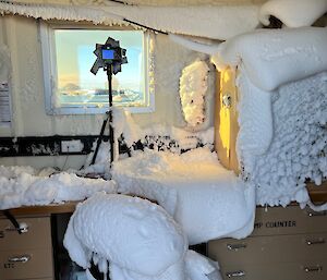 Inside of a science hut showing bench, chair, lab equipment all covered in a layer of snow