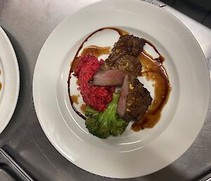 A lamb with a pine nut and pesto crust on a white plate