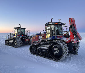 Two tractors parked on a snowy plain under a dim sky with a sunset or sunrise glow on the horizon