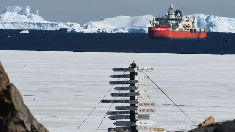 A red ship behind a sign post in the ocean