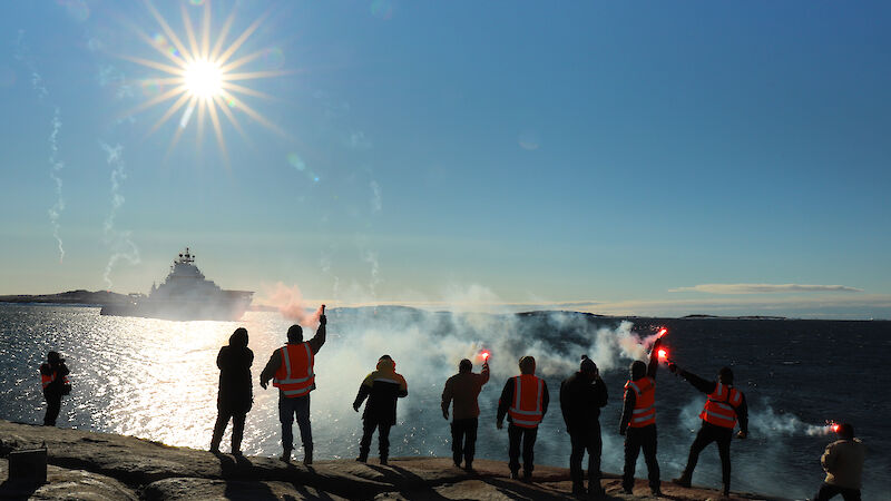 A group of people hold flares with a ship in the background